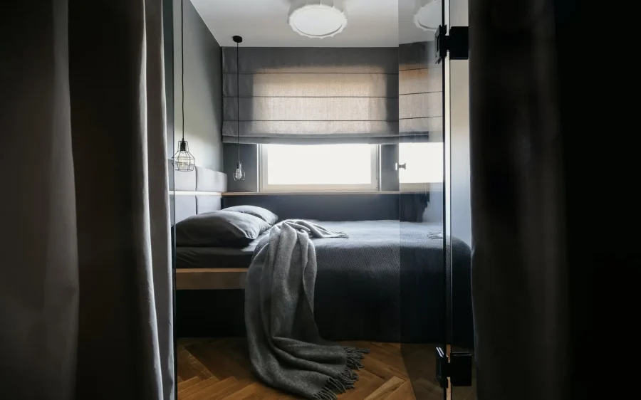 Grey blanket and pillows on bed in simple hotel bedroom interior